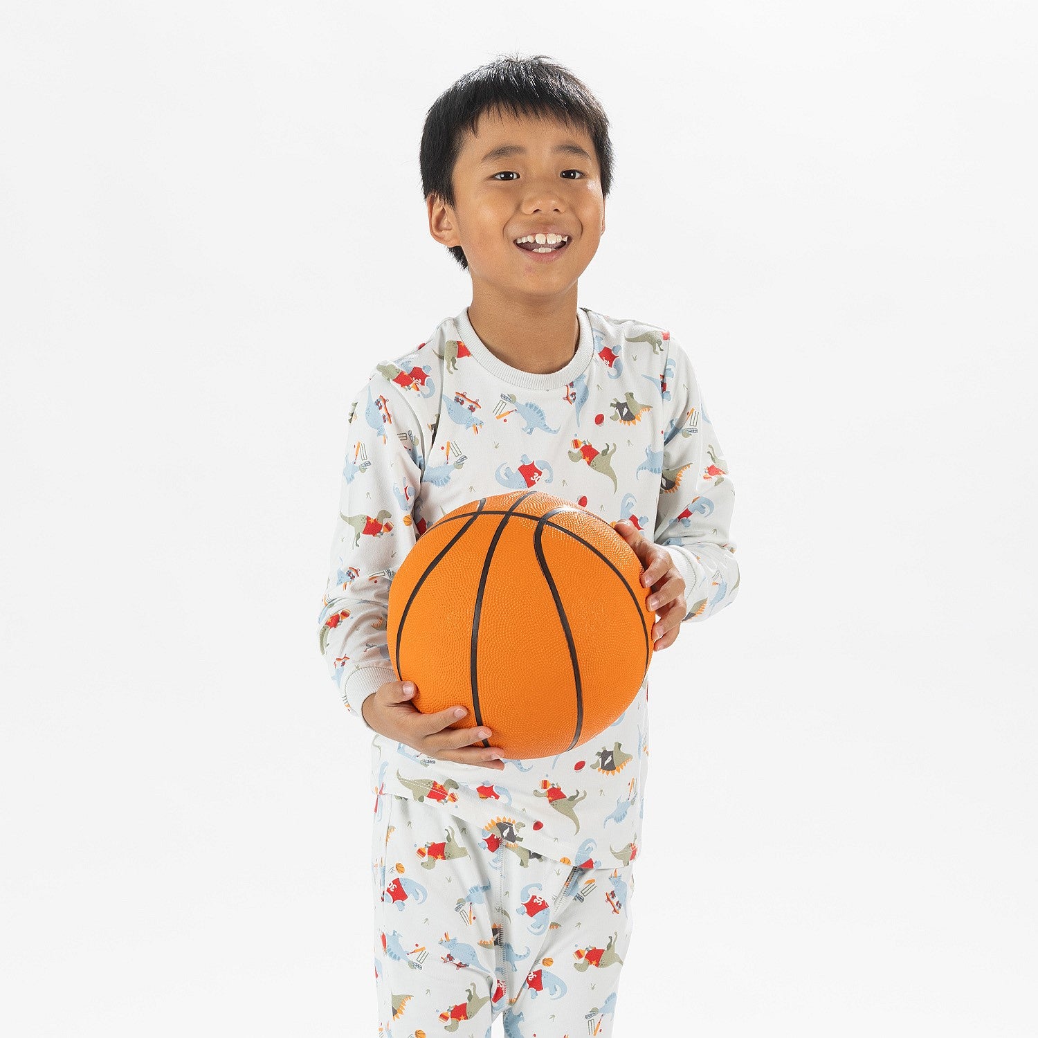 close up bb&b Sleep Kids Dino Sport knit pyjama twosie worn by a child holding a basketball.