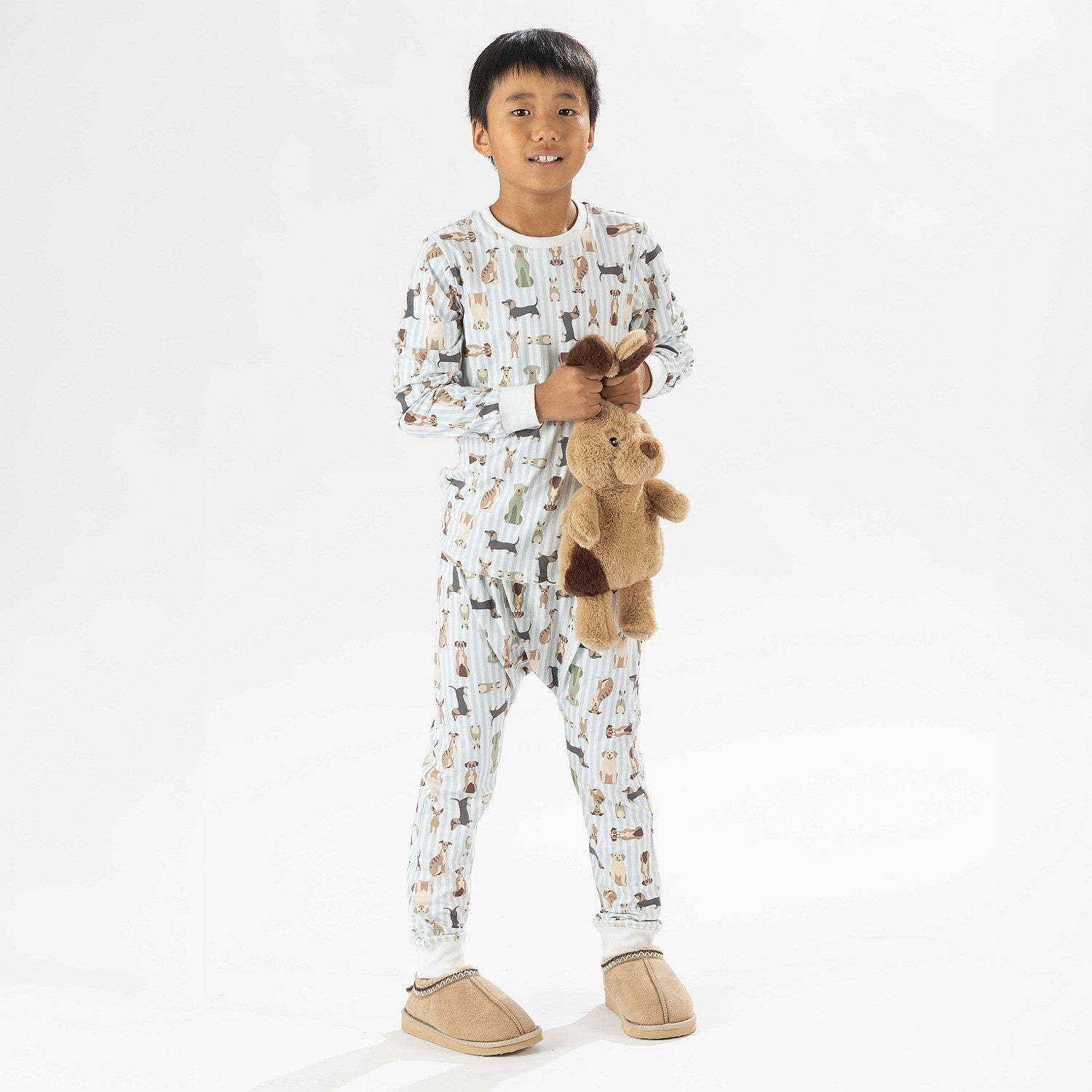 Child wearing bb&b Sleep Kids Dog Stripe knit pyjama twosie while holding a plush dog toy.