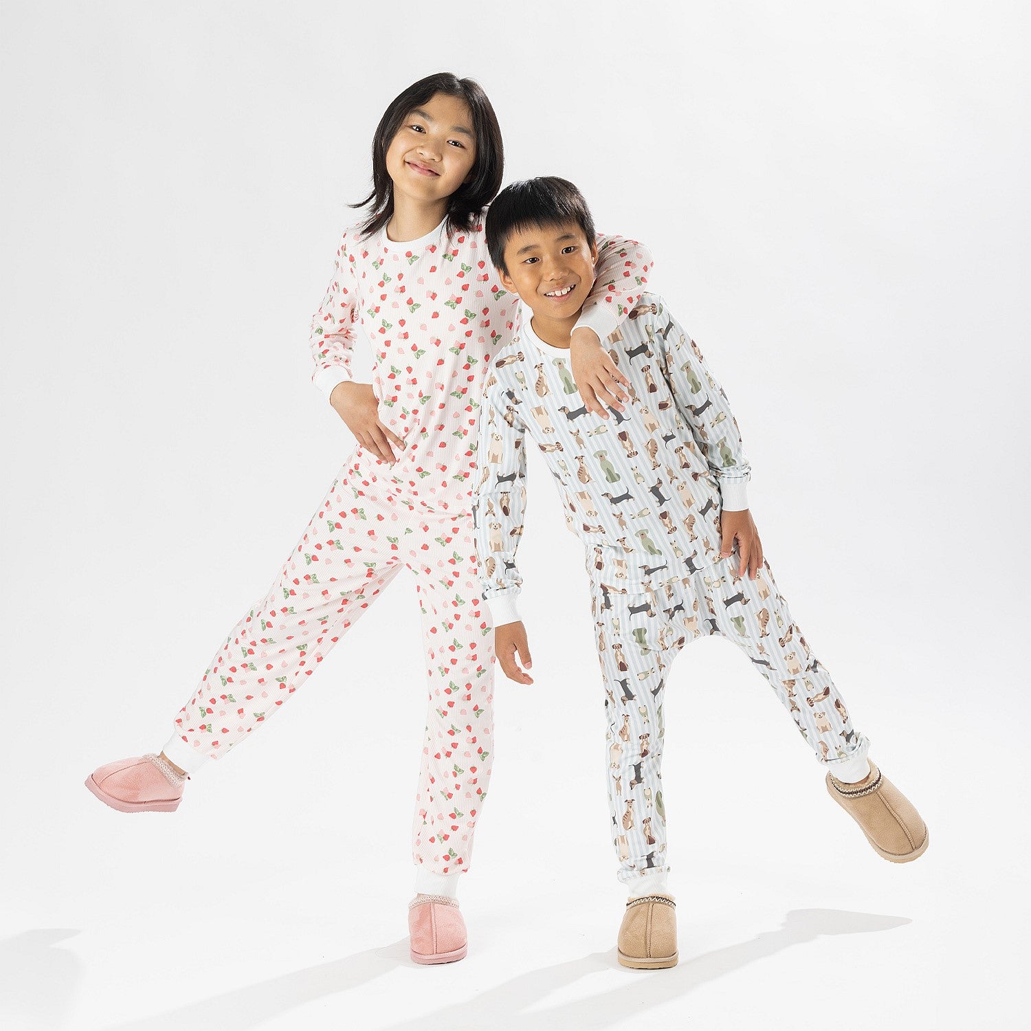 Two children wearing printed pyjama sets, one in pink and one in blue, posing together on a white background.