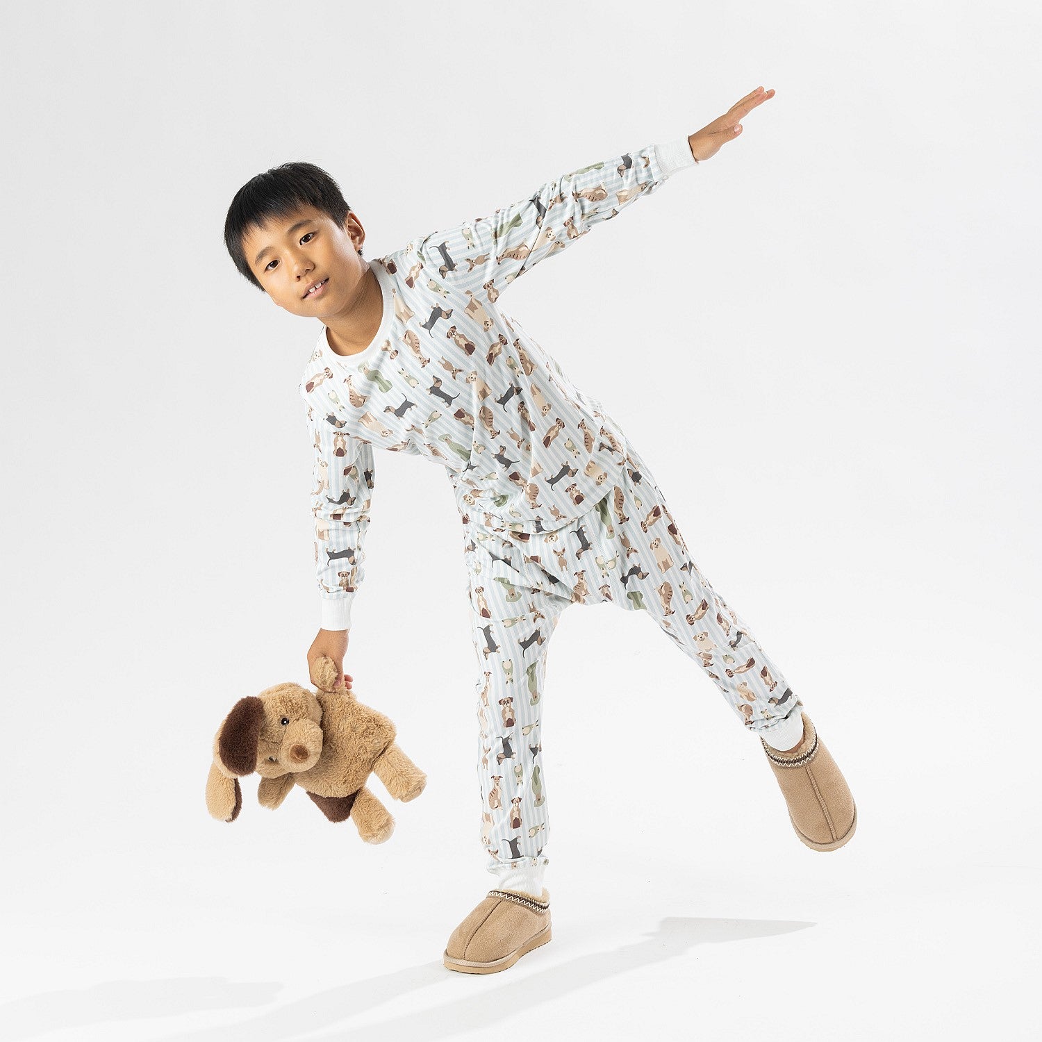 Child wearing bb&b Sleep Kids Dog Stripe knit pyjama twosie while holding a plush dog toy.
