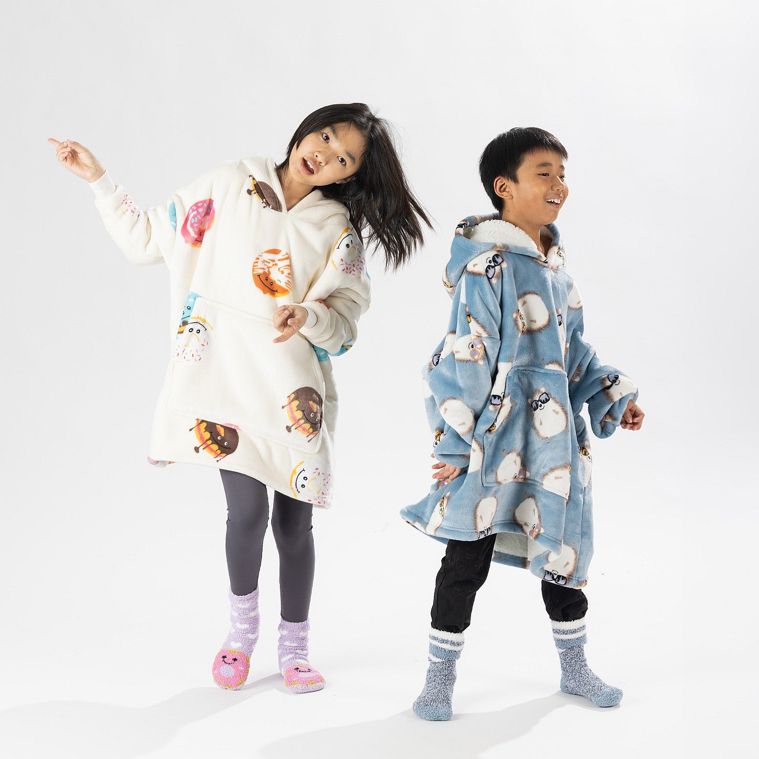 Two children wearing oversized printed hoodies, one in cream and one in blue, standing on a white background.