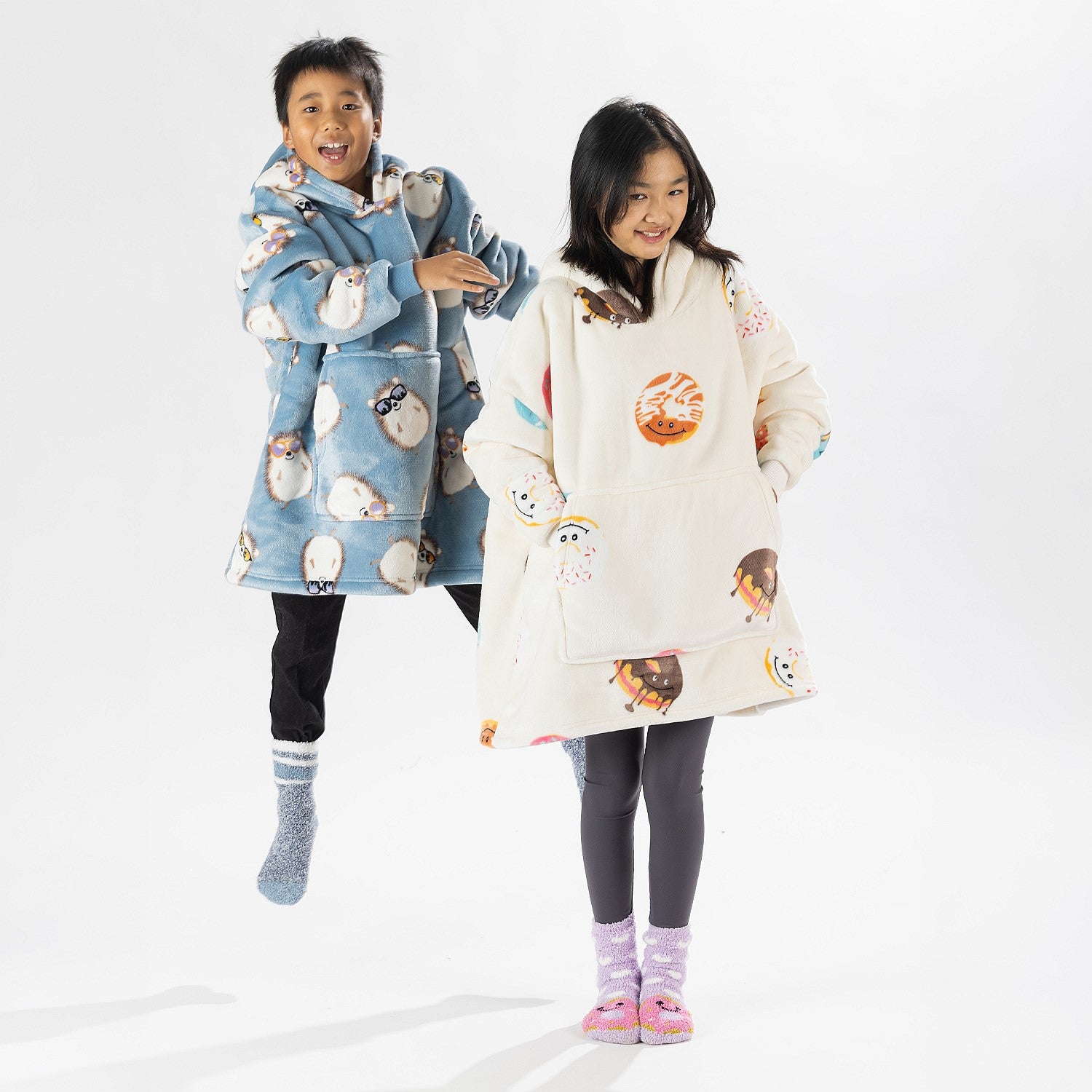 Two children wearing oversized printed hoodies, one in cream and one in blue, standing on a white background.