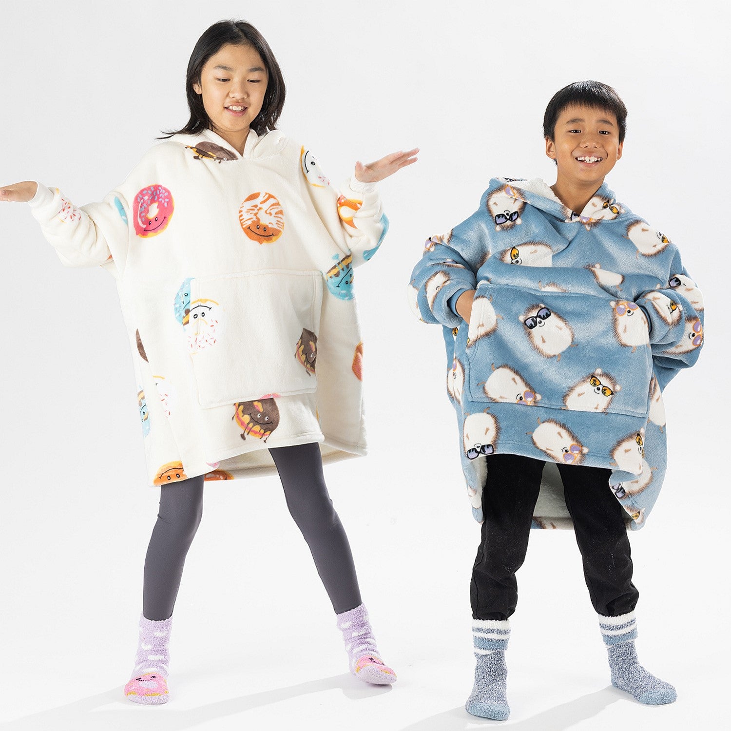 Two children wearing oversized printed hoodies, one in cream and one in blue, standing on a white background.