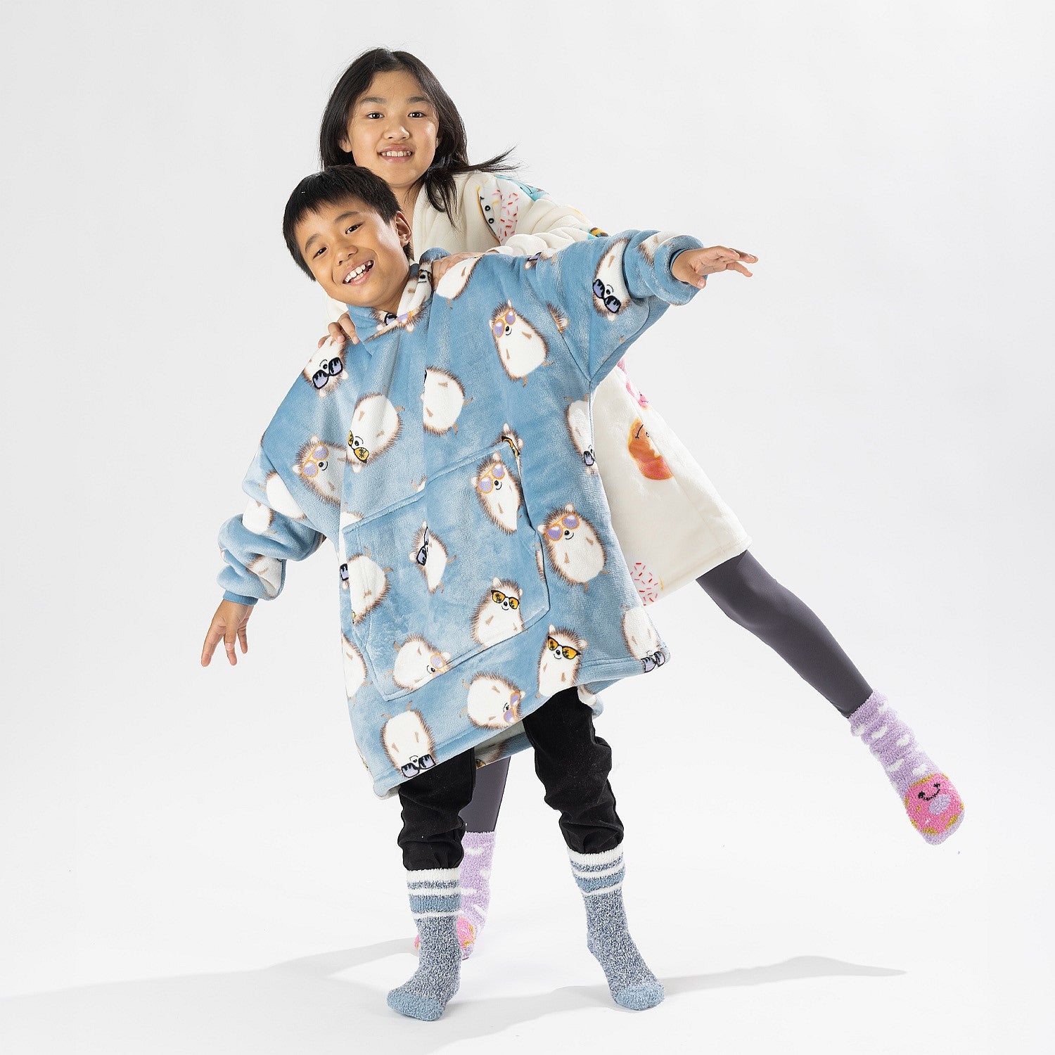 Two children wearing oversized printed hoodies, one in cream and one in blue, standing on a white background.