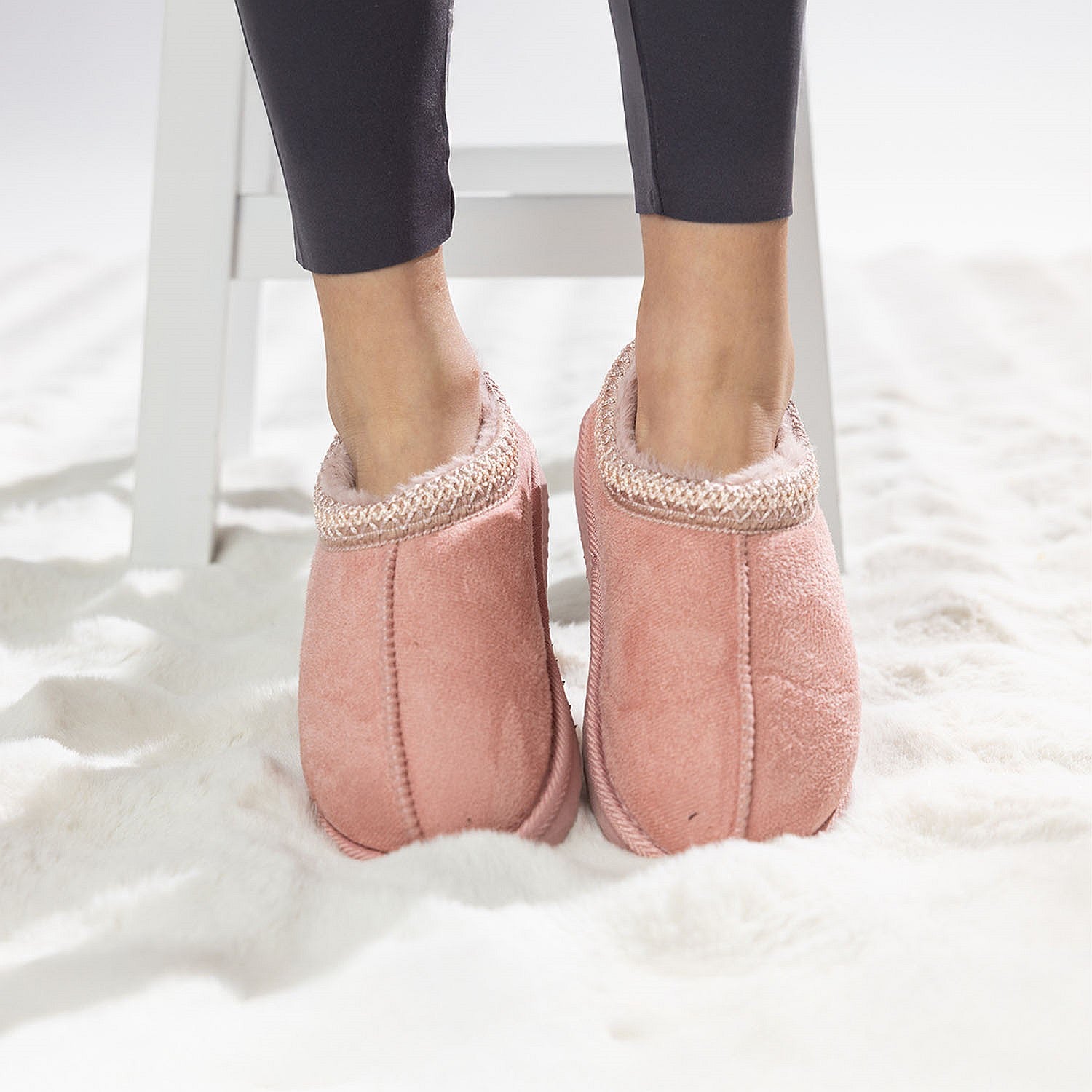 Pink faux fur slippers with soft lining worn on a white rug.