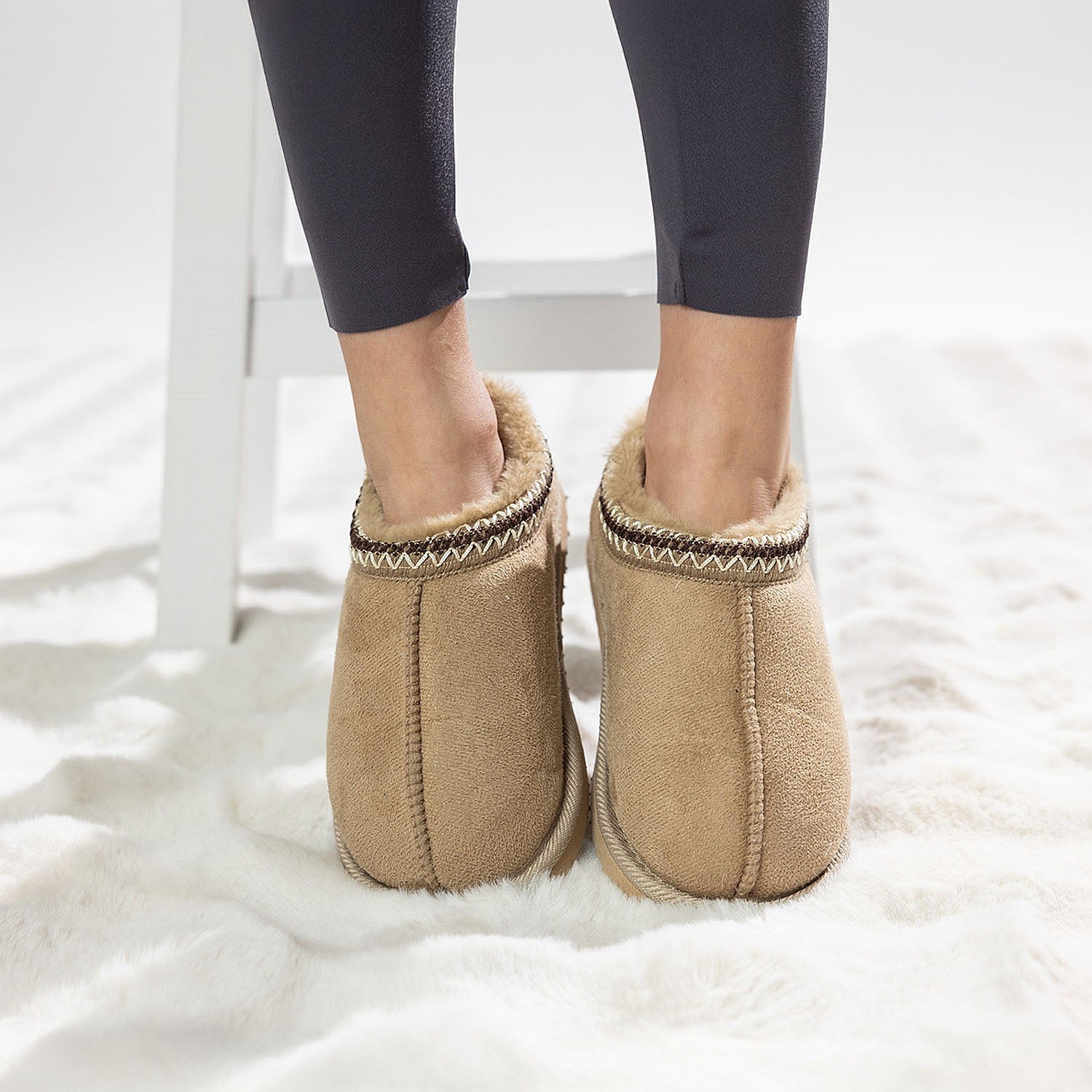 Tan faux fur slippers with soft lining worn on a white rug.
