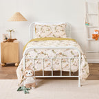 Kid bed styled with natural colour fabric with a delicate leafy vine print in soft green and brown tones. Styled on a white metal bed in a neutral bedroom.