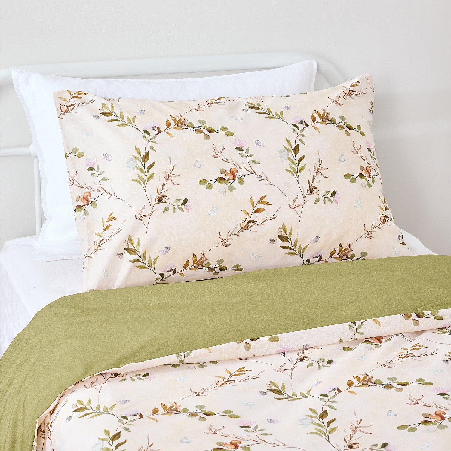 Woodland print pillowcase and duvet cover with a sage green folded edge on a white bed.