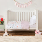 Baby cot styled with a pale pink blanket and soft toys in a neutral nursery room.