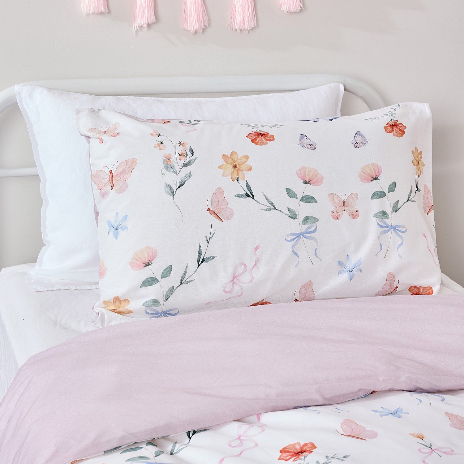 Butterfly print pillowcase and cot cover styled with a soft pink foldover on a white bed.