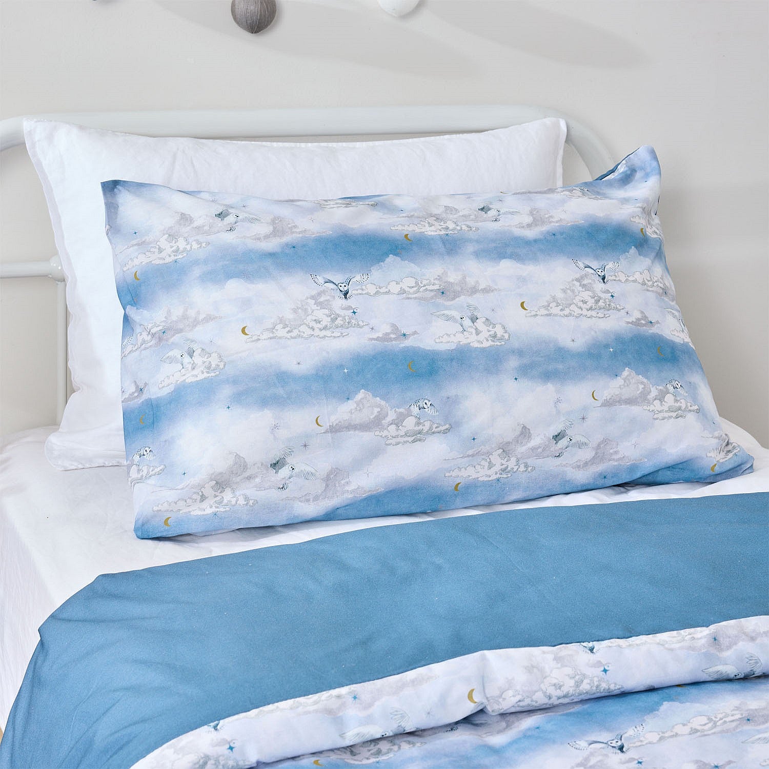 Blue cloud print kids pillowcase and duvet cover styled with a plain blue foldover on a white bed.
