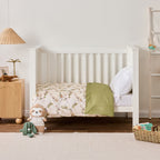 Baby cot styled with natural colour fabric with a delicate leafy vine print in soft green and brown tones. With soft toys in a neutral nursery room.