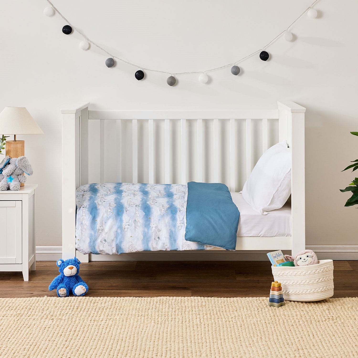 Kids cot styled with a blue cot cover and white pillow in a neutral nursery room.
