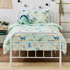 bb&b Kids Dino Beach Party duvet cover set styled on a white metal bed, featuring a mint green dinosaur and beach print with a coordinating pillowcase and plush dinosaur toy.