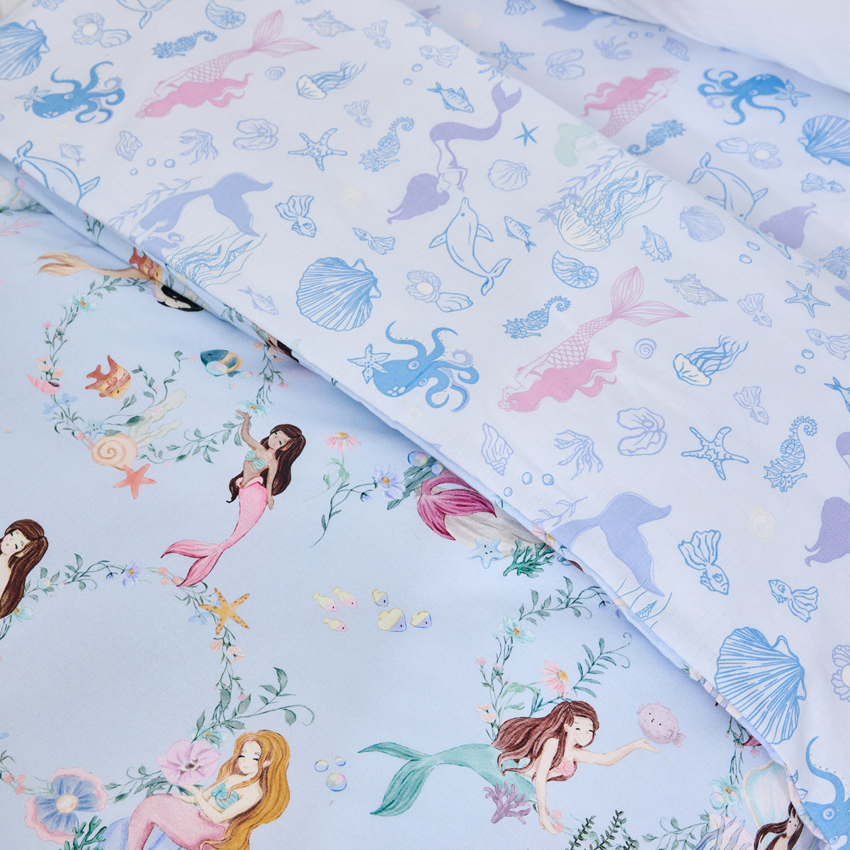 Close-up of the bb&b Kids Mermaid Dreams duvet cover set showing the light blue mermaid print alongside a coordinating pillowcase with shells, octopus, dolphins and underwater motifs.