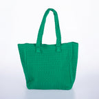 Green woven tote bag with double shoulder straps and textured knitted design on a white background.
