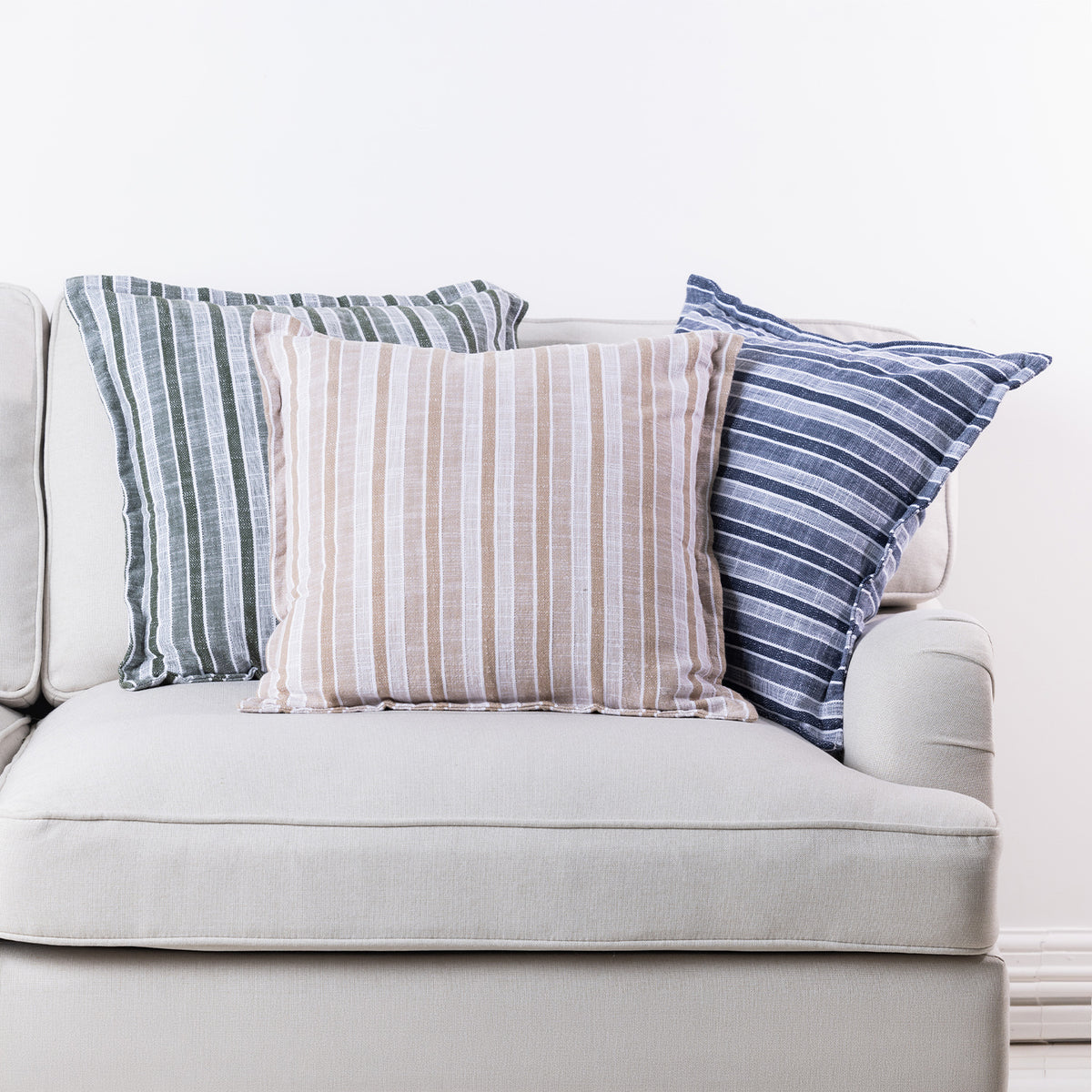 Home Co. Riley striped cushions in Olive, Natural and Navy styled together on a neutral sofa.