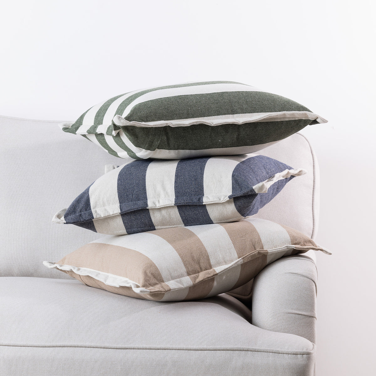 Home Co. Ashley Cushions in Olive, Navy and Natural stacked together on a neutral sofa.