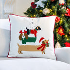 White Christmas cushion featuring four festive dogs stacked together, displayed on a white sofa beside a decorated Christmas tree.