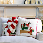 White Christmas Dogs Cushion displayed alongside a red and white candy cane cushion and Santa cushion on a white sofa.
