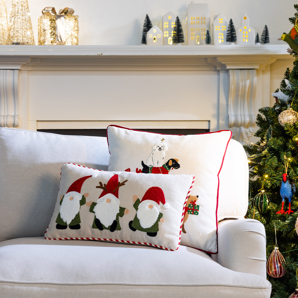 Christmas Gnomes Cushion displayed in front of a Christmas Dogs Cushion on a white sofa beside a decorated Christmas tree.