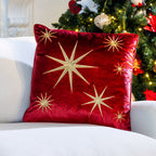 Red velvet Christmas Gold Star Cushion featuring gold embroidered stars, displayed on a white sofa beside a decorated Christmas tree.