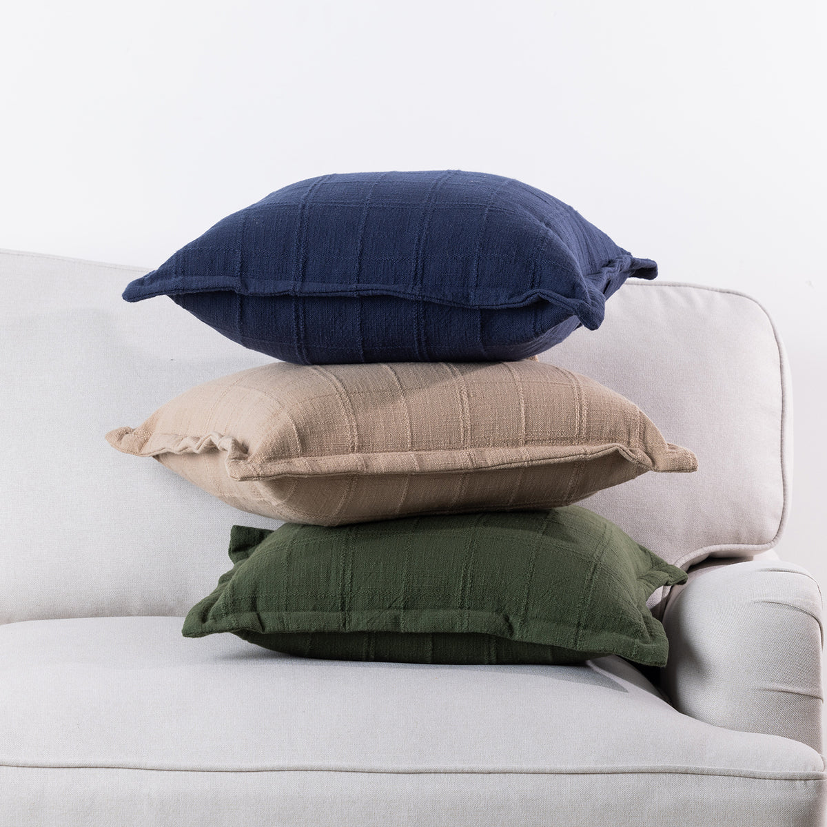 Home Co. Bailey Cushions in Navy, Natural and Olive stacked together on a neutral sofa.