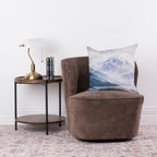 Fieldcrest Aoraki Mount Cook Cushion styled on a brown accent chair beside a wooden side table and brass lamp.