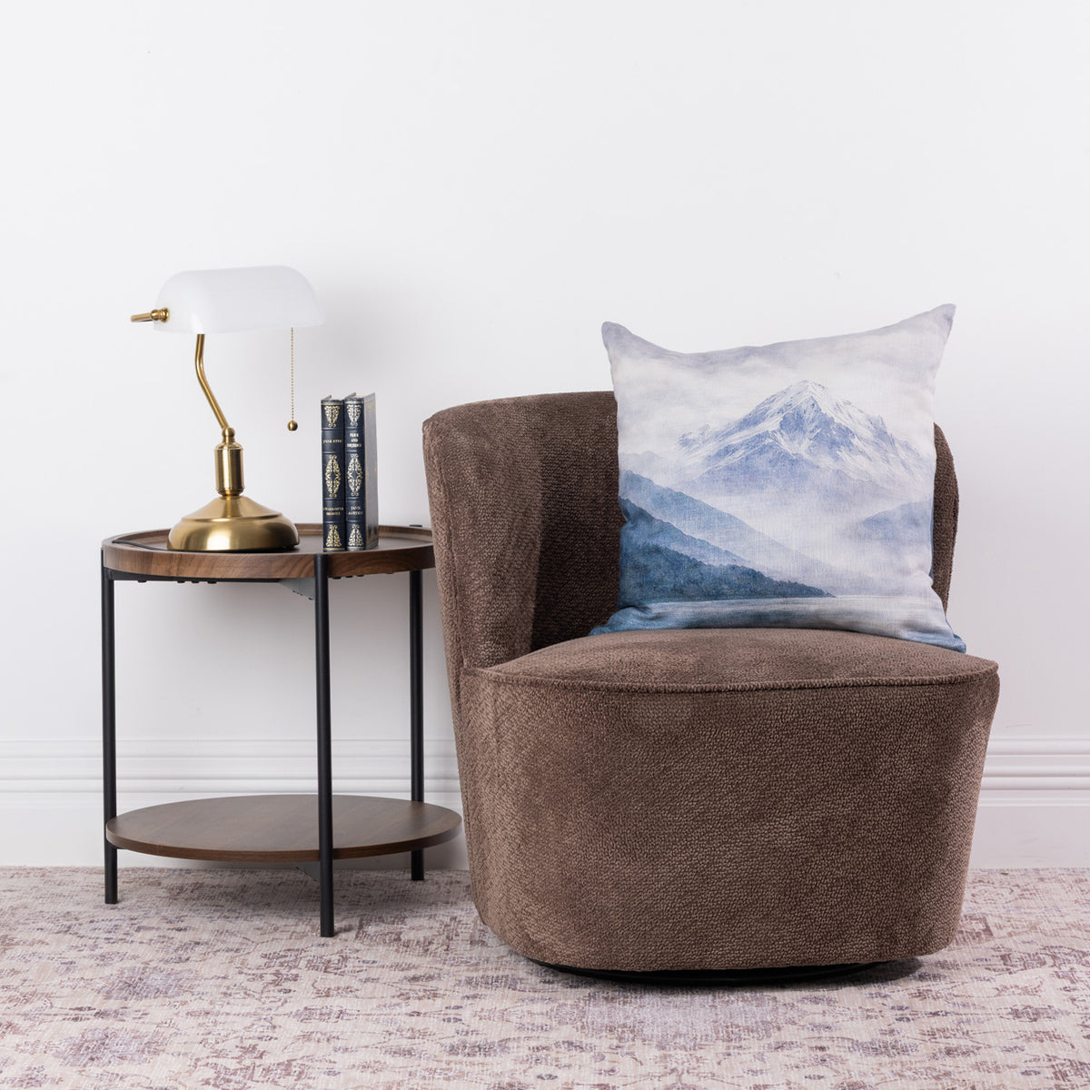 Fieldcrest Aoraki Mount Cook Cushion styled on a brown accent chair beside a wooden side table and brass lamp.