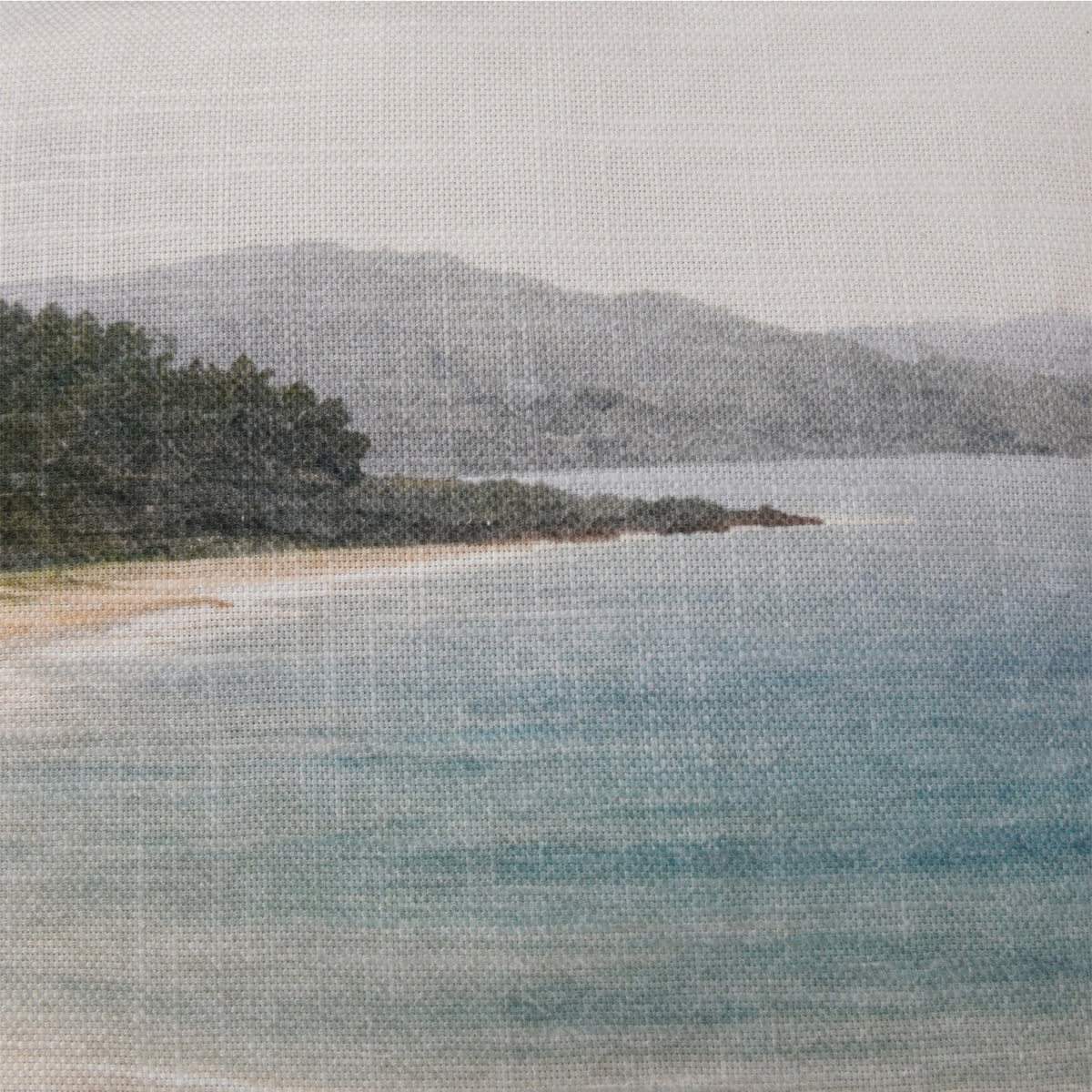 Close-up of the Fieldcrest Serene Coast Cushion showing the woven fabric texture, pale blue water, sandy shoreline and distant hills.