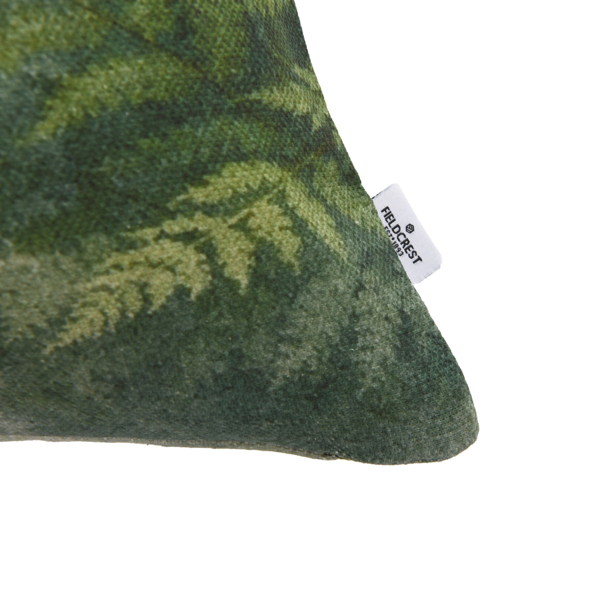 Close-up of the Fieldcrest Northland Forest Cushion corner showing the textured fabric, deep green foliage print and Fieldcrest brand label.