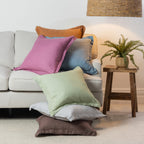 A vibrant collection of linen cushions in soft pastel and earthy tones is casually layered on a neutral sofa, bringing colour, natural texture and relaxed charm to a contemporary living space.