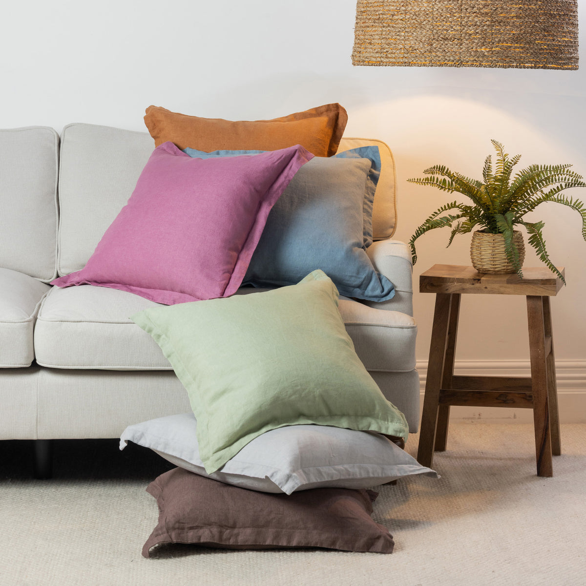 A vibrant collection of linen cushions in soft pastel and earthy tones is casually layered on a neutral sofa, bringing colour, natural texture and relaxed charm to a contemporary living space.