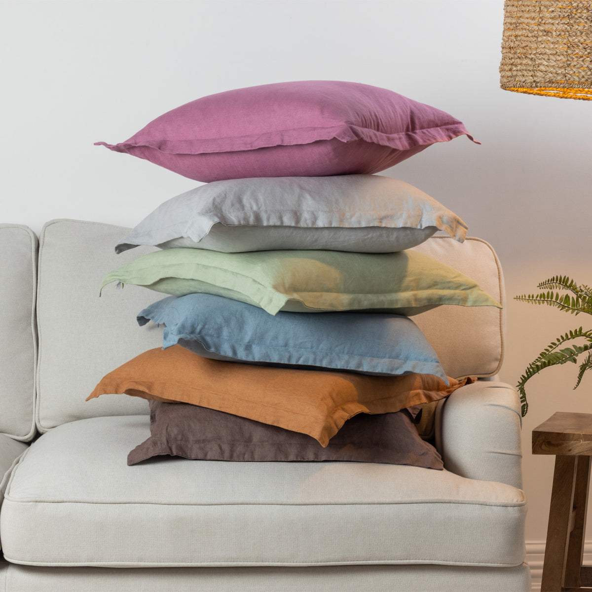 A vibrant collection of linen cushions in soft pastel and earthy tones is casually layered on a neutral sofa, bringing colour, natural texture and relaxed charm to a contemporary living space.