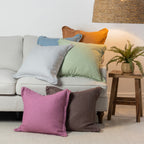 A vibrant collection of linen cushions in soft pastel and earthy tones is casually layered on a neutral sofa, bringing colour, natural texture and relaxed charm to a contemporary living space.