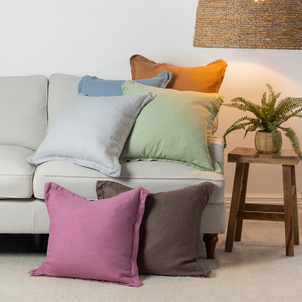 A vibrant collection of linen cushions in soft pastel and earthy tones is casually layered on a neutral sofa, bringing colour, natural texture and relaxed charm to a contemporary living space.