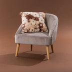 Amparo Macey Cushion in blush, styled on a grey chair with a soft faux fur spotted design.