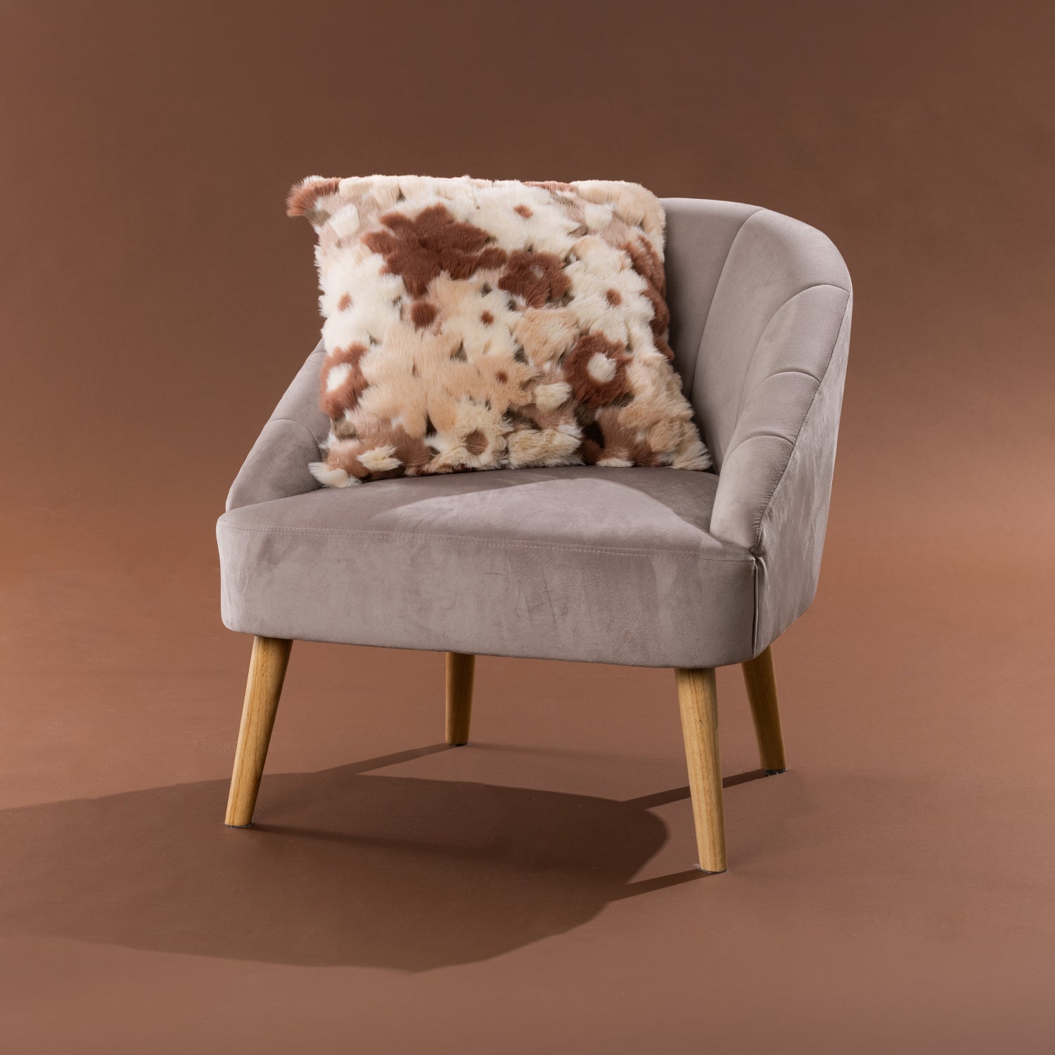 Amparo Macey Cushion in blush, styled on a grey chair with a soft faux fur spotted design.