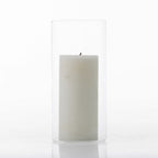 White pillar candle displayed inside a tall clear glass cylinder vase on a white background.