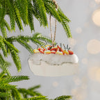 Slice of pavlova Christmas ornament topped with colourful fruit and fluffy cream hanging from a Christmas tree branch.