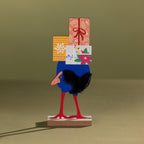 Decorative wooden kiwi figurine carrying colourful wrapped gifts against an olive green backdrop.