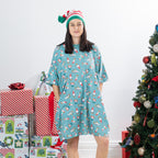 Woman wearing the Christmas Wishes Christmas Gnome Sleep Tee in jade with an all-over festive gnome print, styled with a striped Christmas hat beside wrapped presents and a decorated Christmas tree.