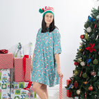 Woman modelling the Christmas Wishes Christmas Gnome Sleep Tee in jade beside wrapped presents and a decorated Christmas tree.