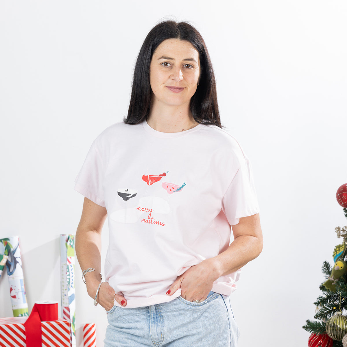 Front view of woman wearing the Christmas Wishes Merry Martinis Tee in pink, showing the relaxed short-sleeve fit and festive chest graphic.