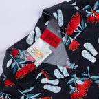 Close-up of the black Christmas Wishes kids festive shirt collar and label, showing the pōhutukawa flower and jandal print.