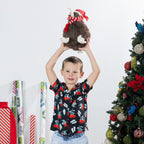 Young boy wearing the black Christmas Wishes kids festive shirt while holding a Christmas plush toy overhead.