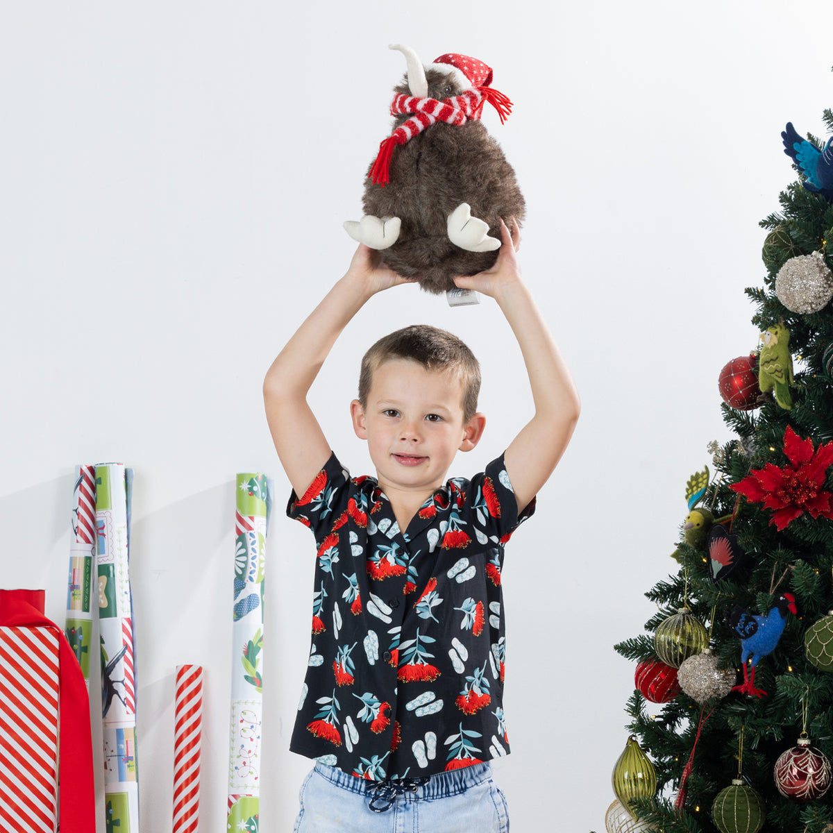 Young boy wearing the black Christmas Wishes kids festive shirt while holding a Christmas plush toy overhead.
