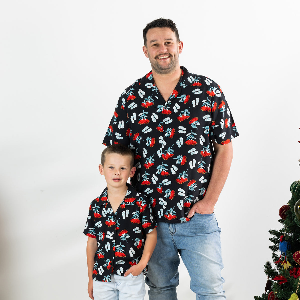 Young boy and adult man wearing matching black Christmas Wishes pōhutukawa festive shirts.