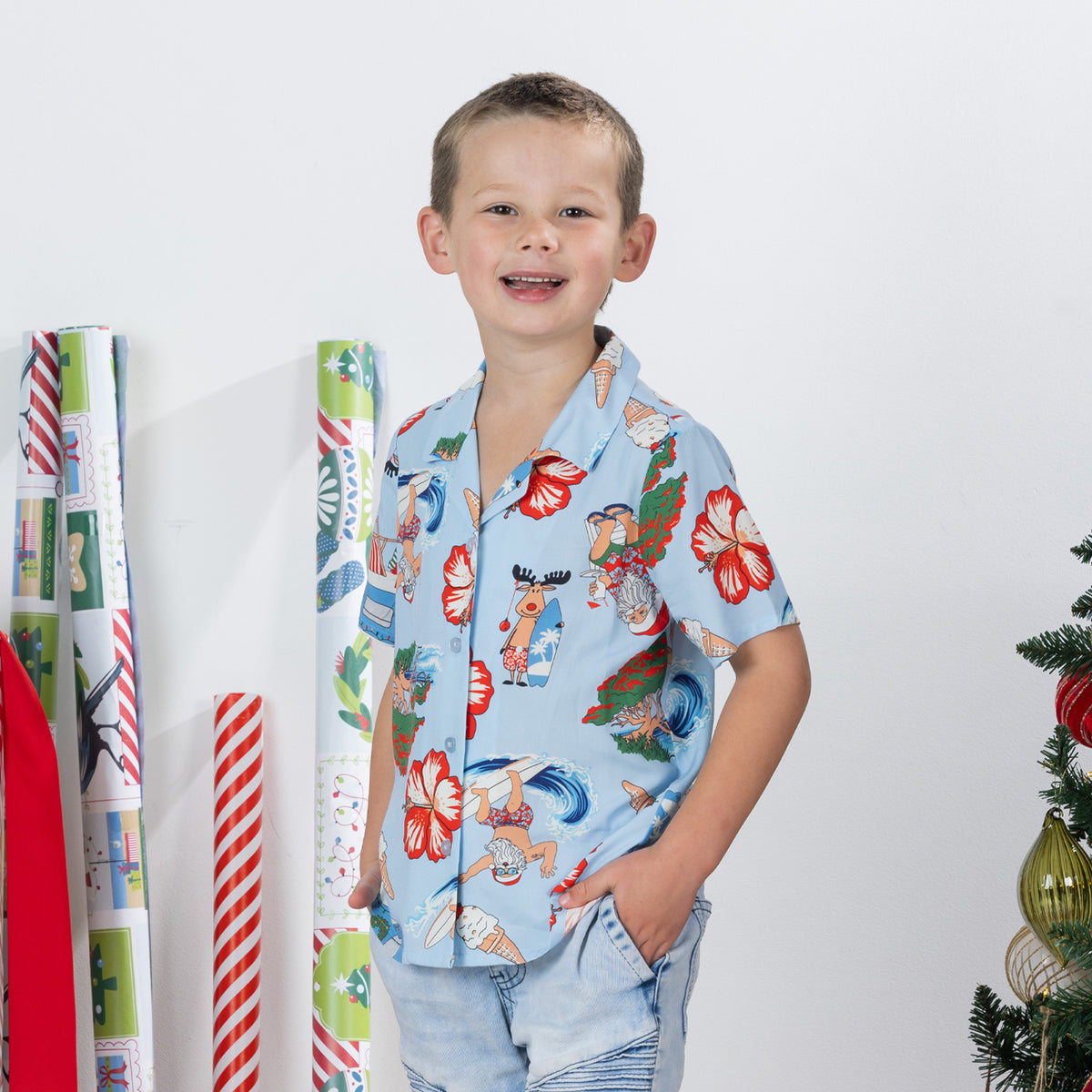Young boy wearing the faded blue Christmas Wishes kids Cheeky Santa festive shirt with denim shorts.
