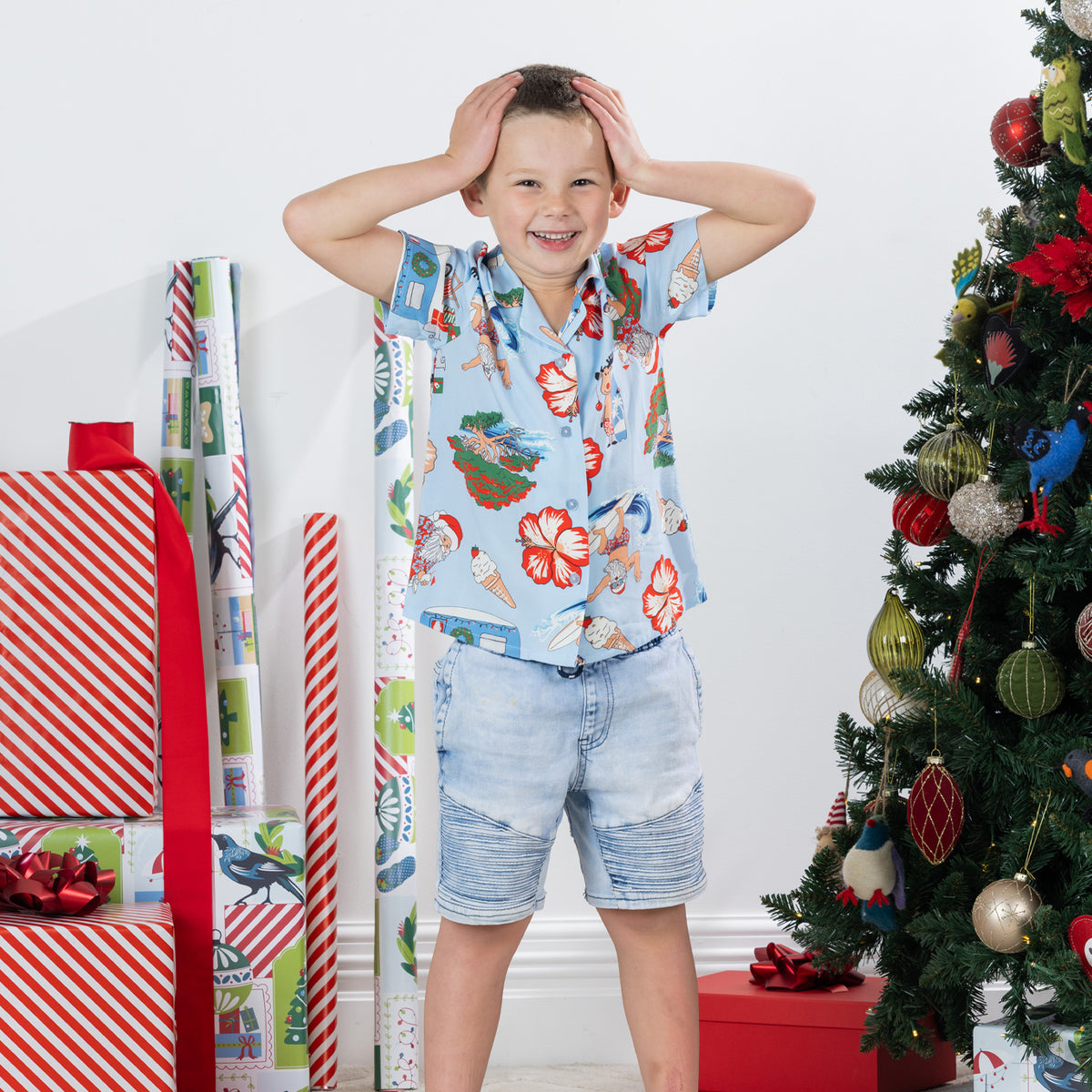 Young boy wearing the faded blue Christmas Wishes kids Cheeky Santa festive shirt in a playful Christmas setting.